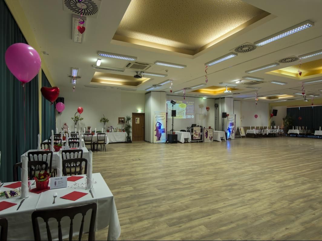 Large banquet hall with tables, balloons, and a few people near the back wall