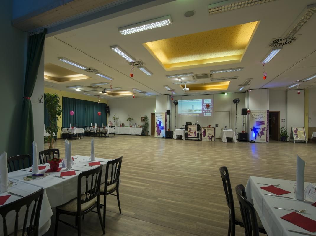 Spacious banquet hall with tables, chairs, ceiling lights, and a polished wood floor
