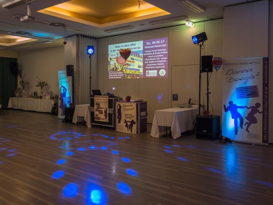 Event hall with projected presentation, tables, and blue stage lighting on the floor.