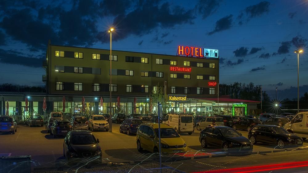 Nighttime view of a lit hotel with parked cars in front and a neon “HOTEL” sign