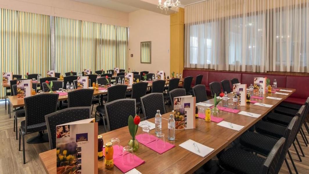 Banquet hall set with long tables, black chairs, pink napkins, and menus before a formal event