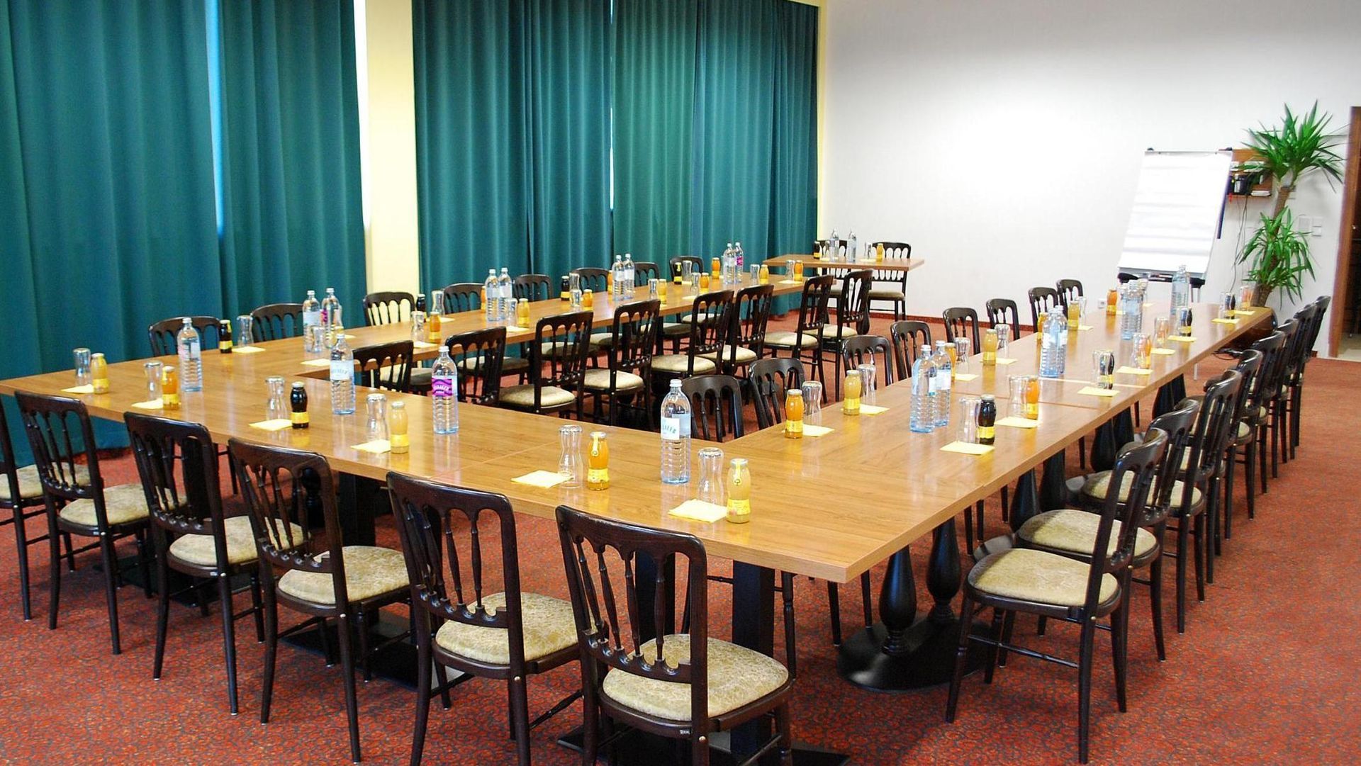 Conference room with a long U-shaped table set with glasses and chairs, teal curtains in back.