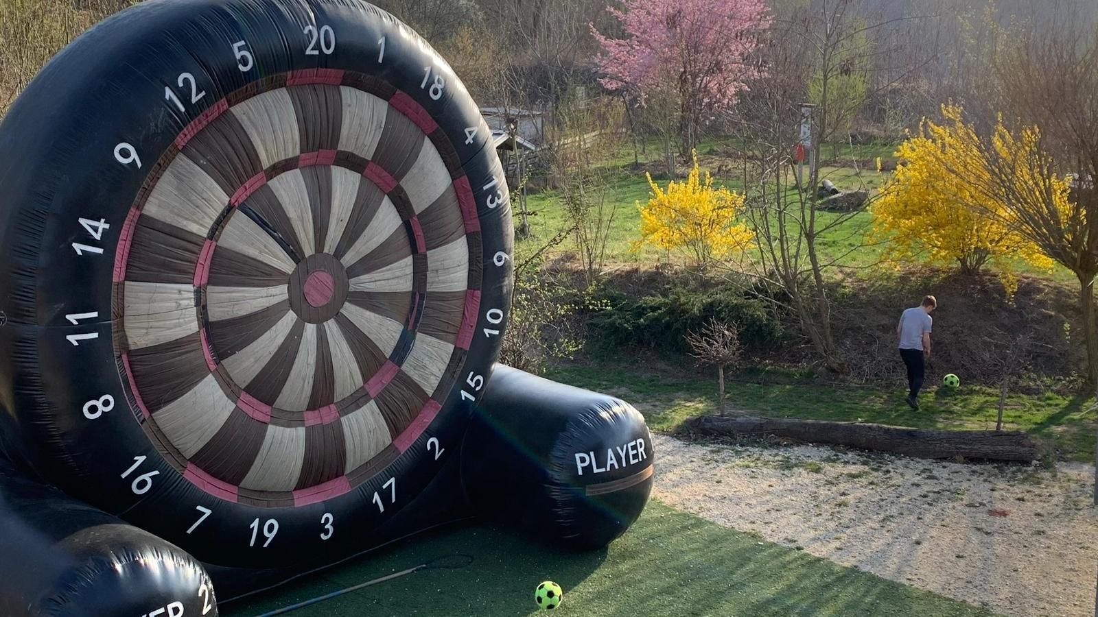 Giant outdoor dartboard game by a garden path, with autumn trees and a person in the background.