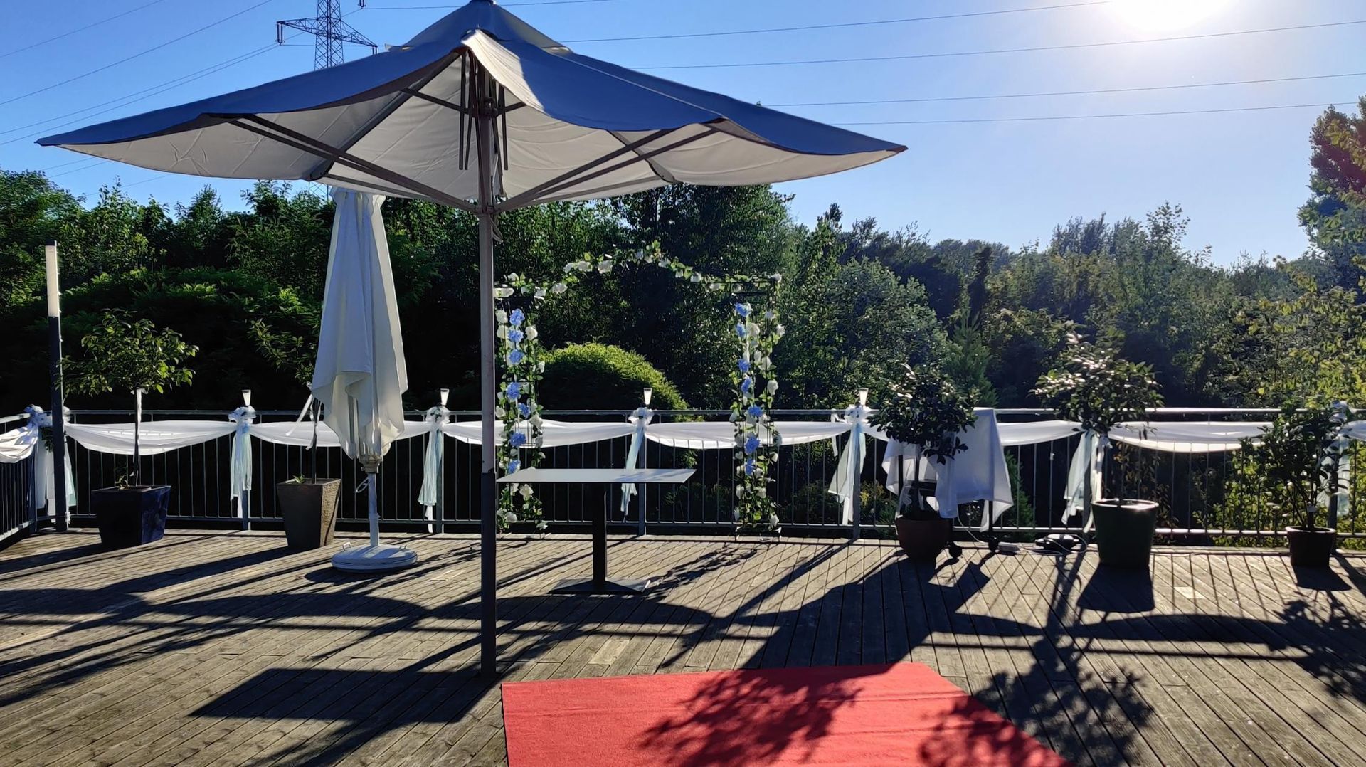 Outdoor patio with white umbrellas, tables, and chairs on a sunny deck with a red carpet runner