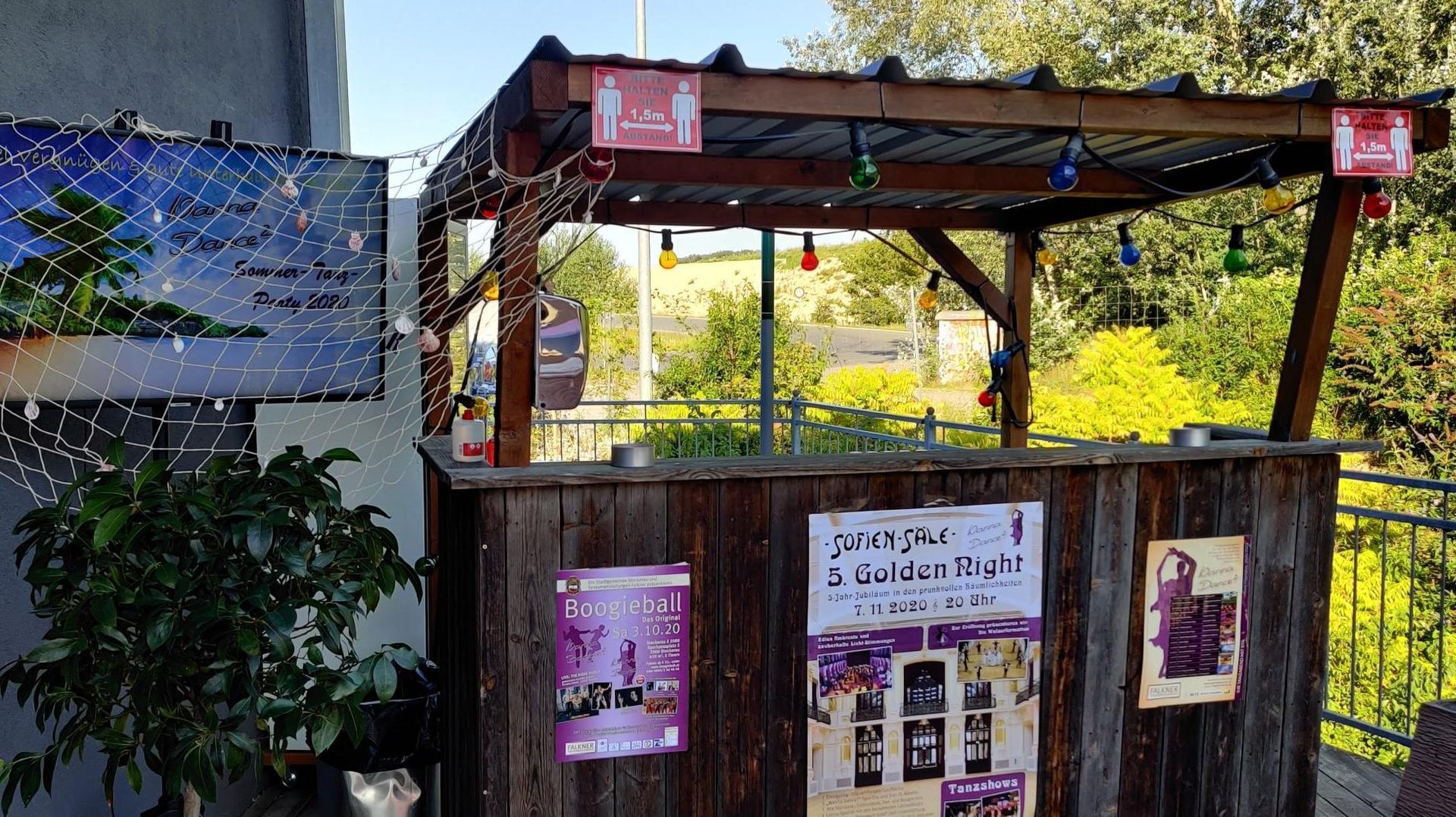Rustic outdoor kiosk with pink signs and posted notices beside a plant-covered wall