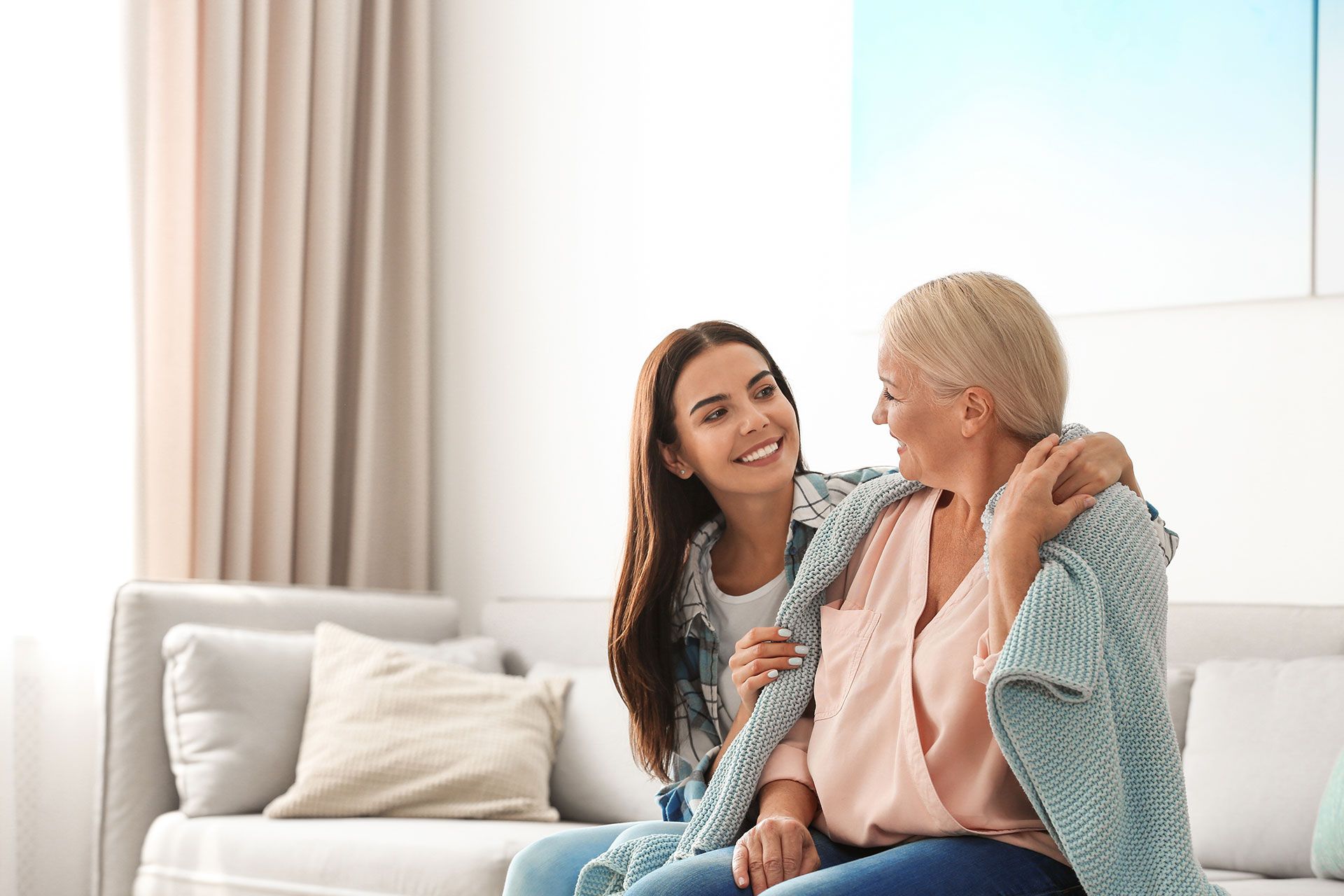 Eine junge Frau sitzt mit einer älteren Frau auf einer Couch.