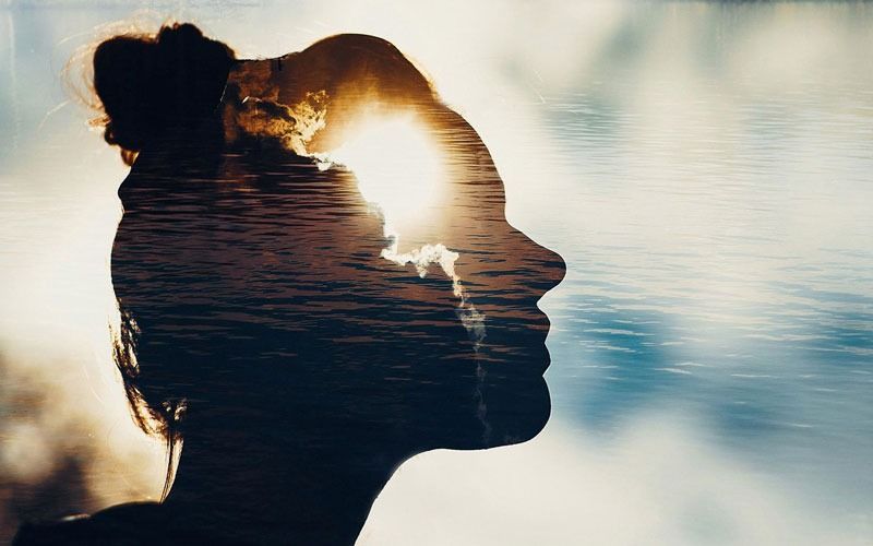 Una doble exposición de la cabeza de una mujer con el sol brillando a través de sus ojos.