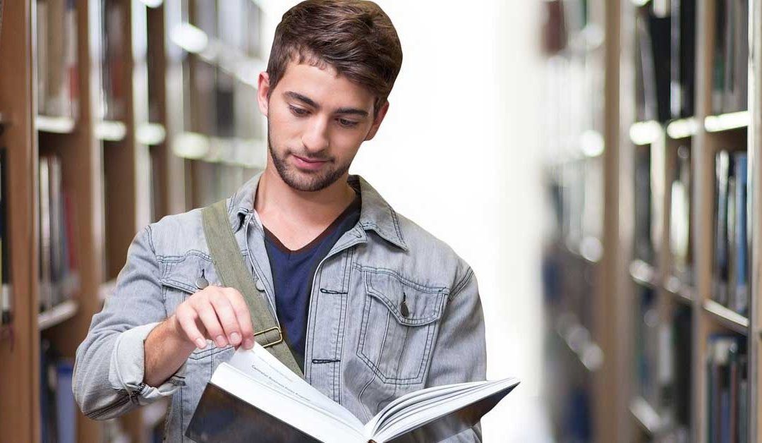 Un hombre está leyendo un libro en una biblioteca.