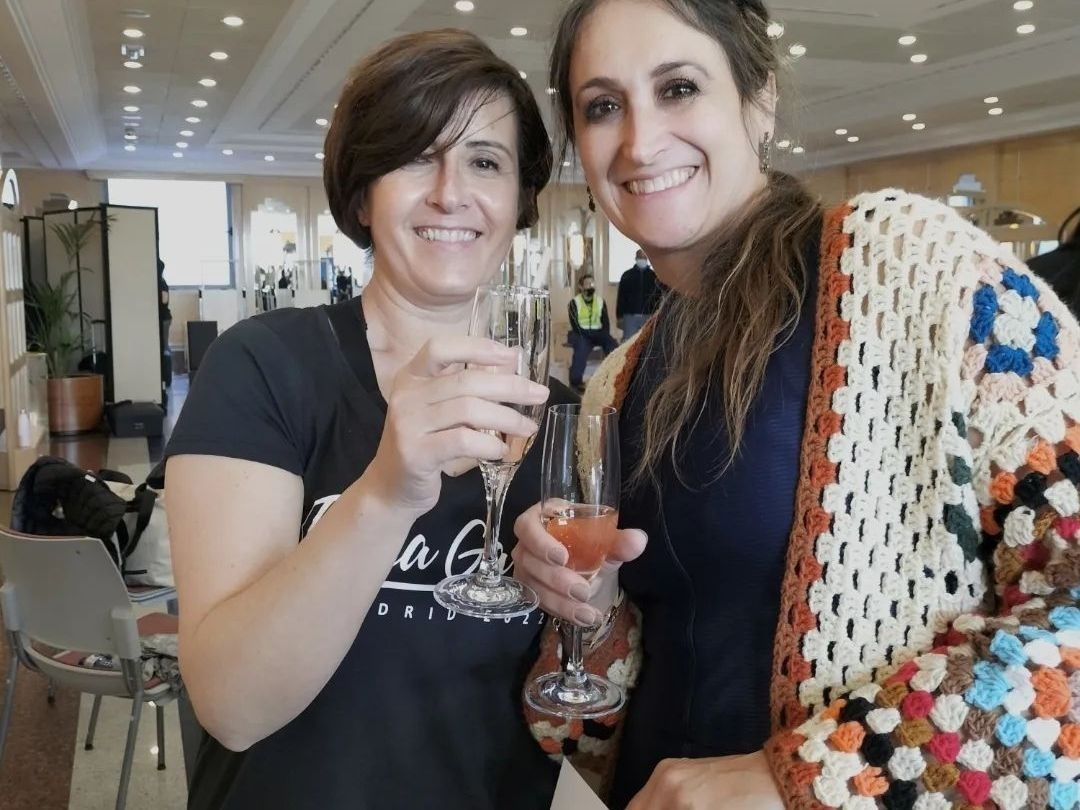 Dos mujeres sostienen copas de vino y sonríen a la cámara.