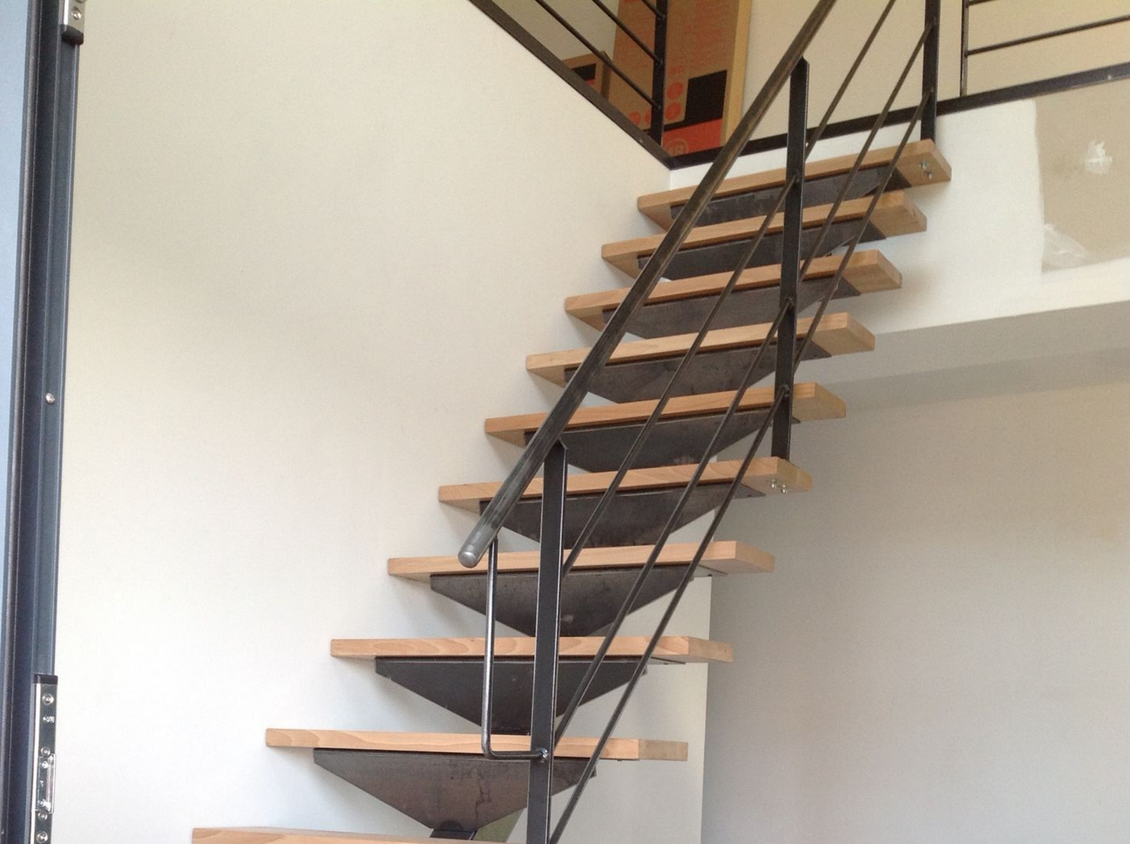 Escalier moderne avec marches en bois, rampes noires et poutres industrielles apparentes.