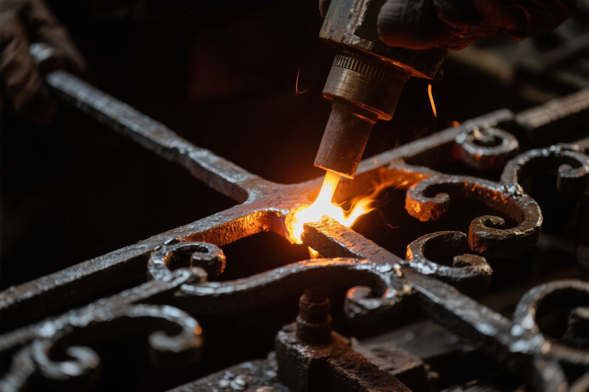 Le chalumeau d'un soudeur découpe des volutes métalliques incandescentes sur un portail en fer sombre.