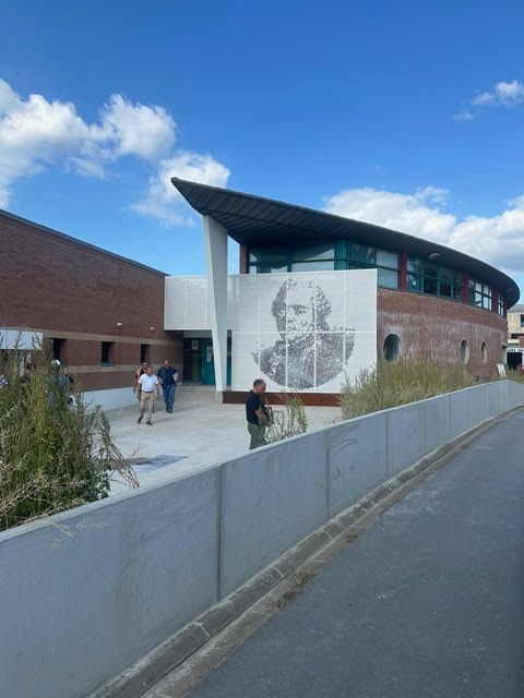 Bâtiment moderne orné d'une fresque, passants à l'extérieur, sous un ciel bleu nuageux