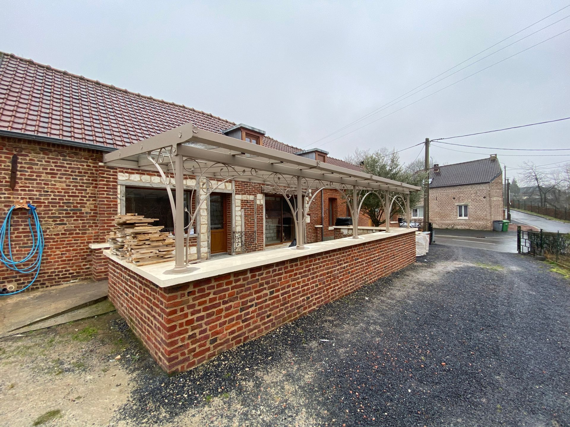 Patio moderne dans un jardin paysager, agrémenté d'une pergola noire, de sièges en osier et d'une cheminée extérieure en pierre.