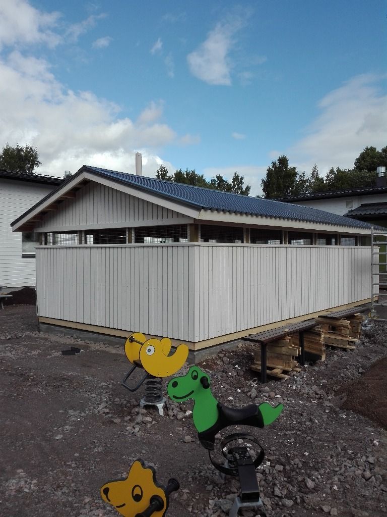 Valkoinen vajan kaltainen rakennelma, jossa on aaltopeltivuoraus, soratontilla pilvisen taivaan alla.