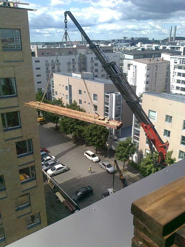 Rakennusnosturi nostaa puupalkkia kaupungin sisäpihan yli kerrostalojen välissä