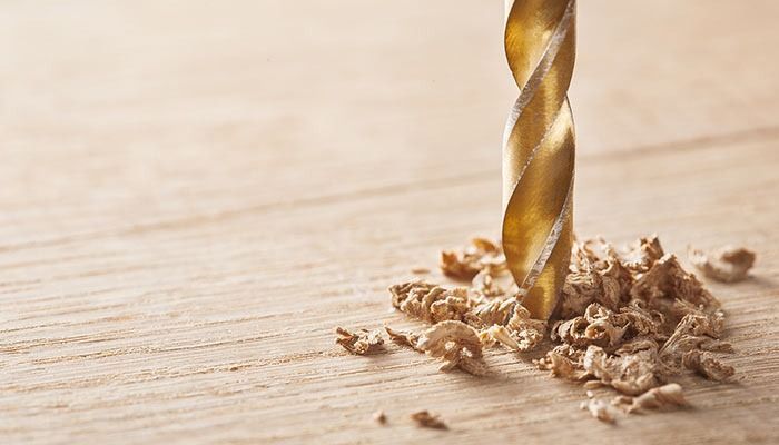 Lähikuva poranterästä, joka poraa vaaleaa puuta, ja sen ympärillä on käpristyneitä puulastuja.