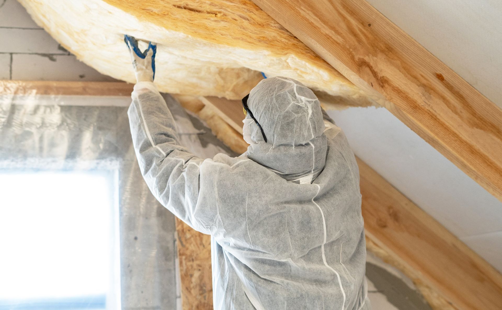 Un homme en combinaison de protection isole le plafond d'une maison.