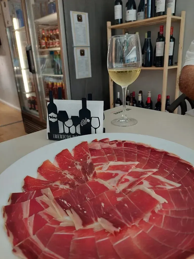 Jamón curado en lonchas finas sobre un plato blanco con una copa de vino blanco en un restaurante.