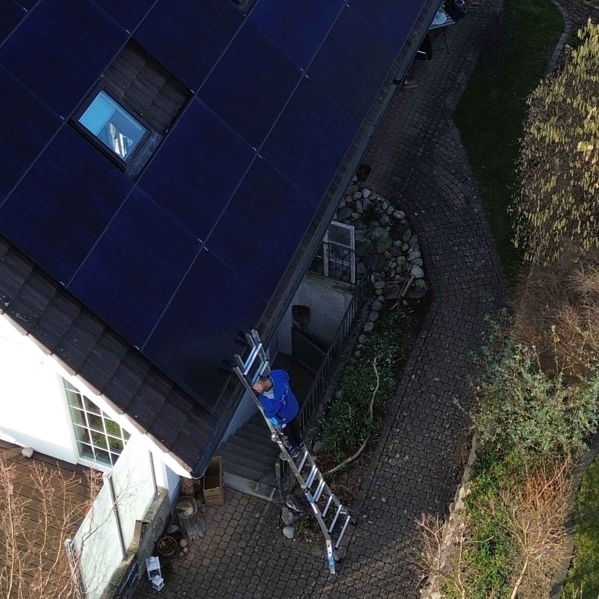 Eine Luftaufnahme eines Mannes auf einer Leiter, der an einem Solarpanel auf dem Dach eines Hauses arbeitet.