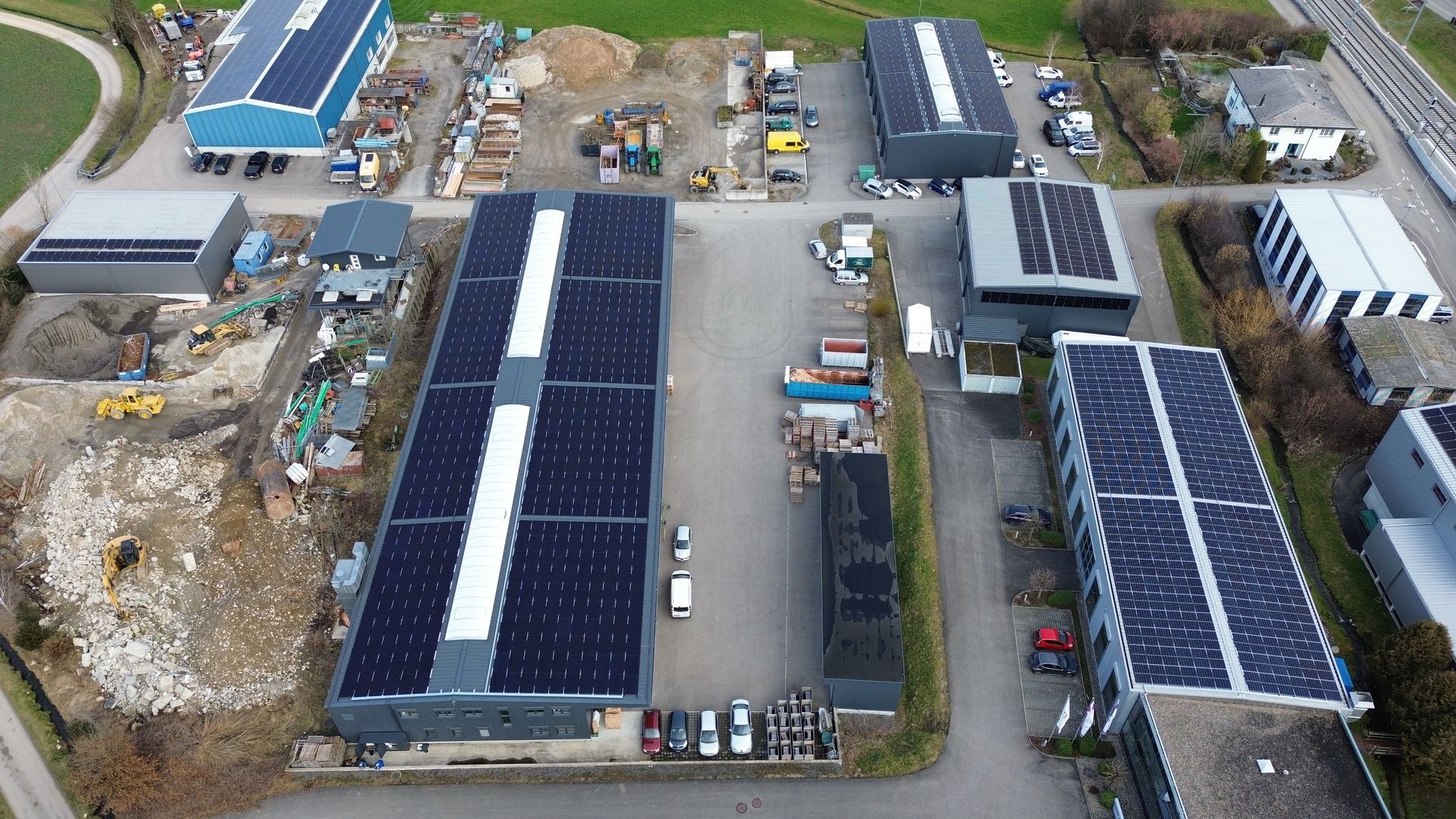 Mehrere Industriehallen mit großflächigen Solaranlagen auf den Dächern, umgeben von Fahrzeugen