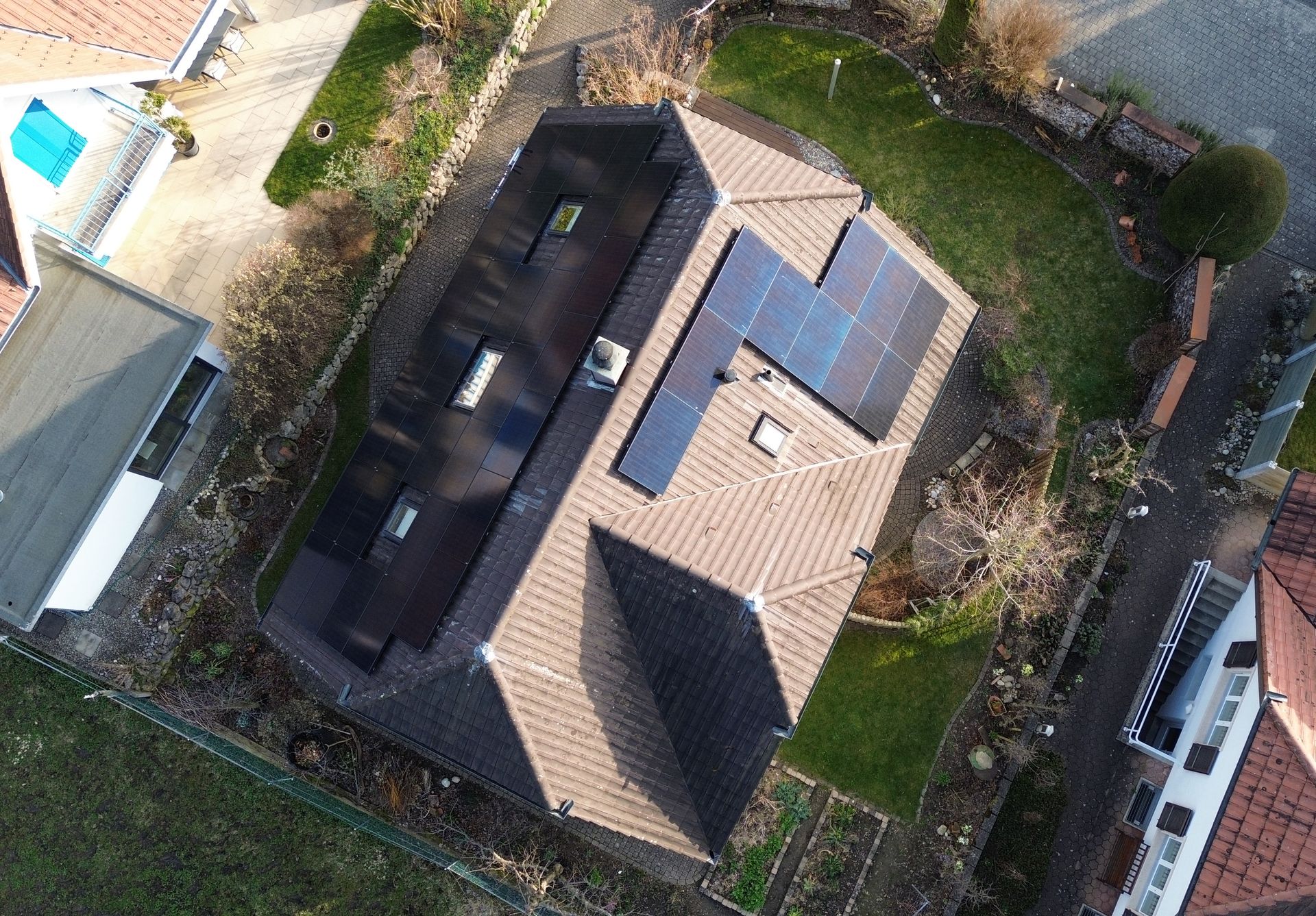 Luftaufnahme eines Wohnhauses mit Ziegeldach und Solarpaneelen umgeben von Garten und Nachbarhäusern
