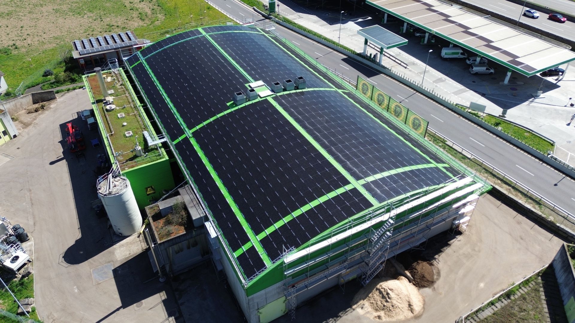
Luftaufnahme eines Industriegebäudes mit großflächigen Solarpanels auf dem Dach neben