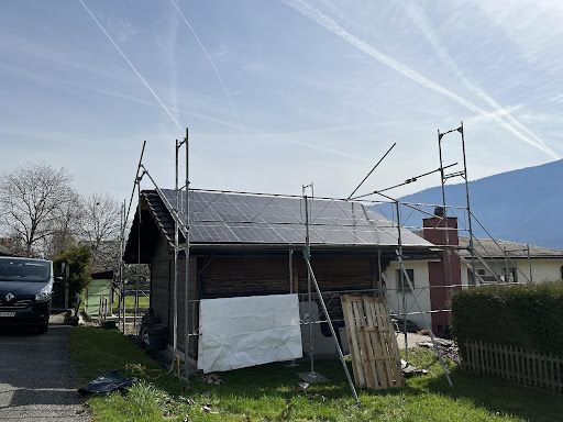 Industriehalle mit Solarmodulen auf dem Dach, umgeben von Parkplätzen, Straßen und weiteren Gebäuden