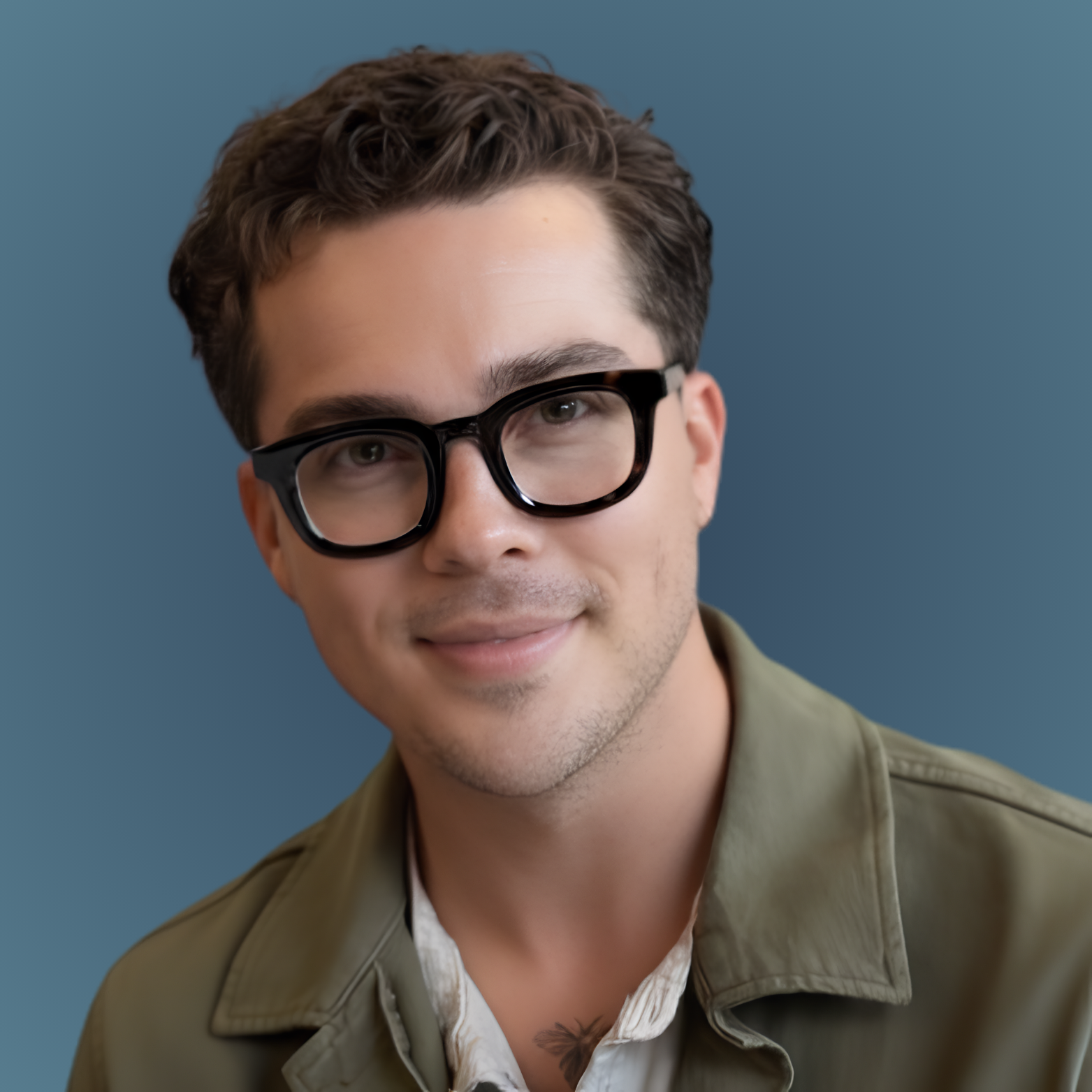 Man with black glasses and olive jacket smiling against a blue background