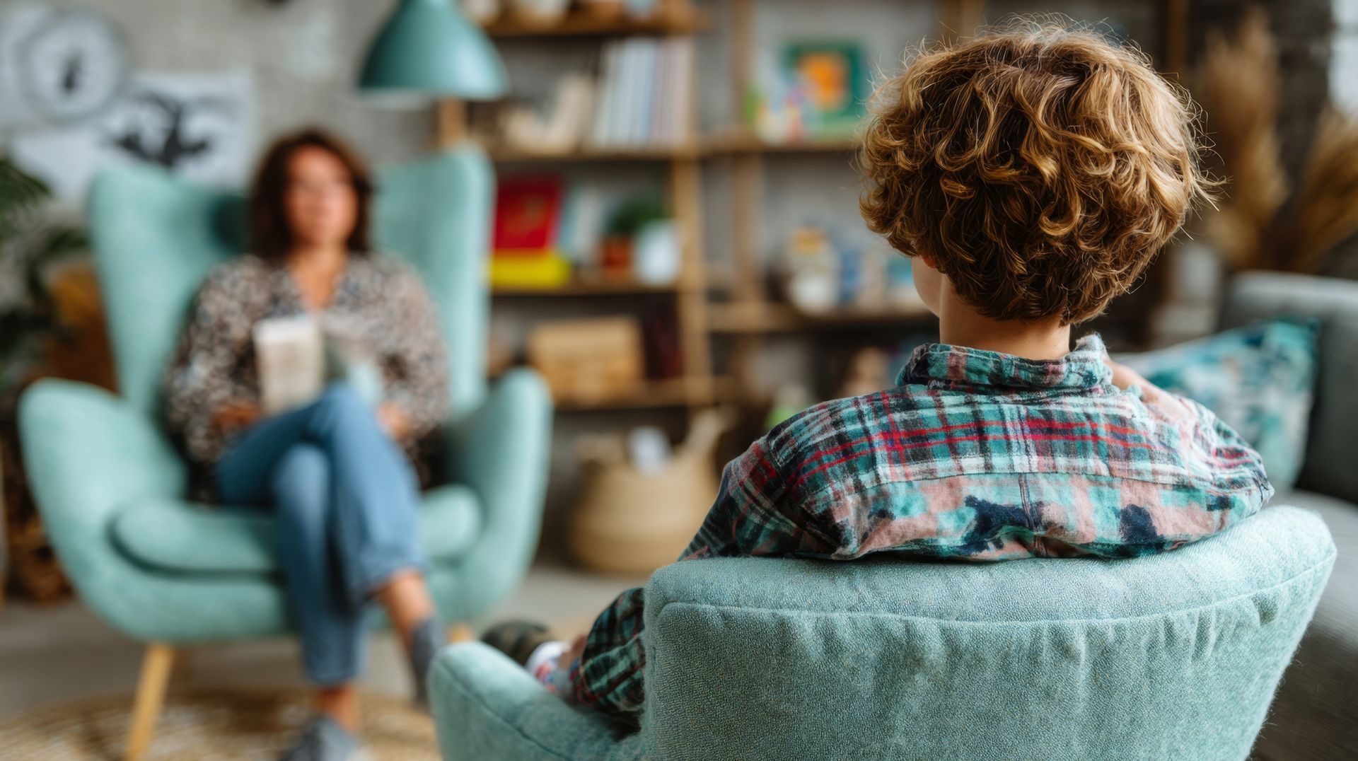 Deux personnes dans un salon confortable, l'une assise dans un fauteuil turquoise face à l'autre en arrière-plan.