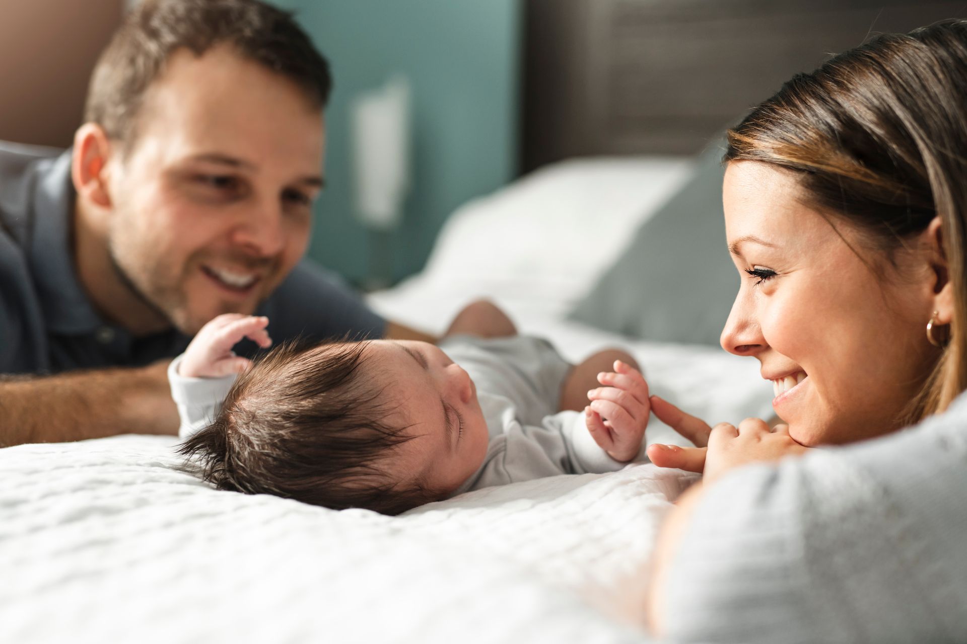 Des parents sourient à leur nouveau-né allongé sur un lit.