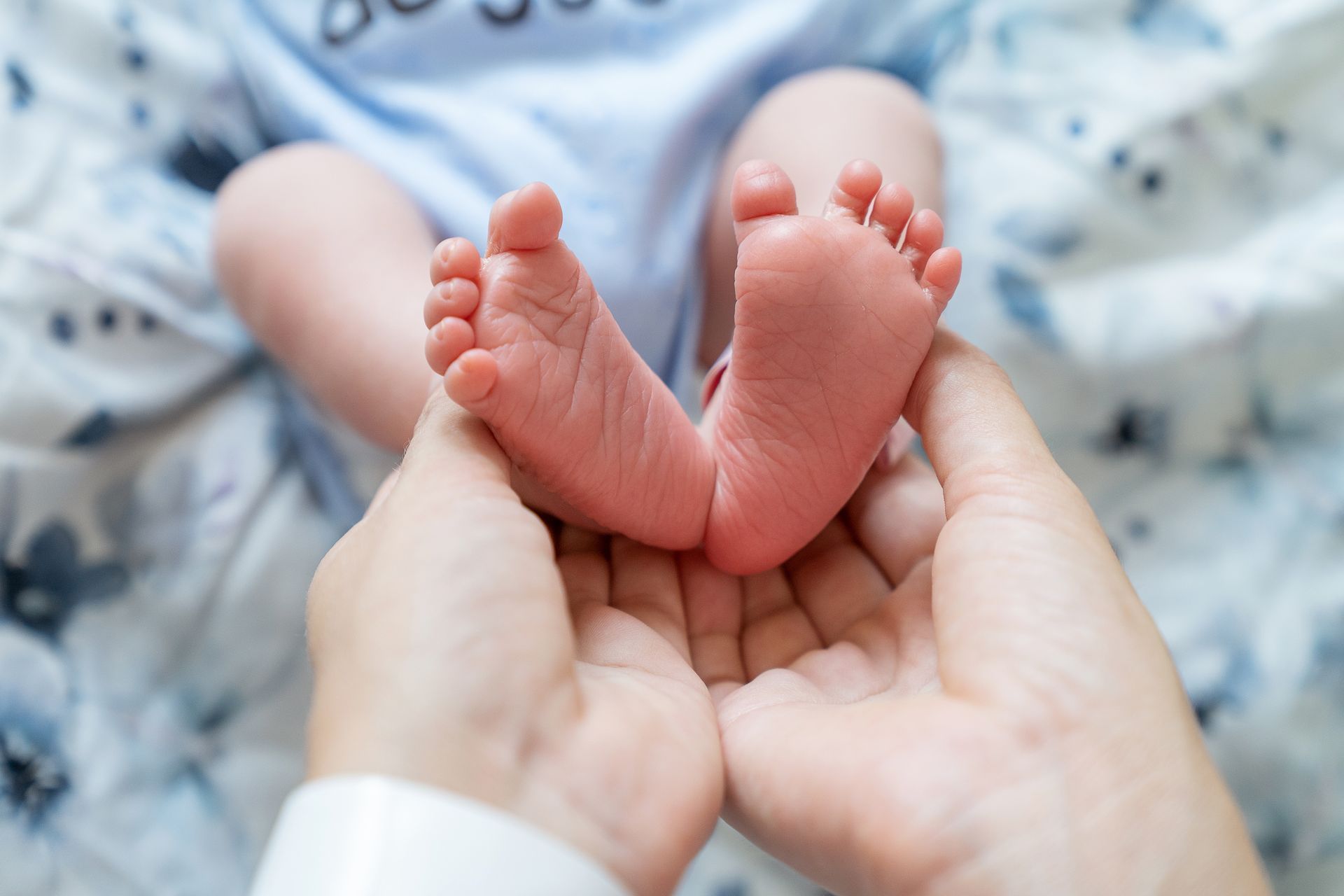 Les pieds d'un nouveau-né délicatement tenus dans les mains d'un adulte sur une couverture douce