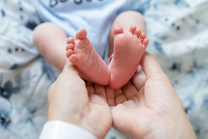 Les pieds d'un nouveau-né délicatement tenus dans les mains d'un adulte sur une couverture douce