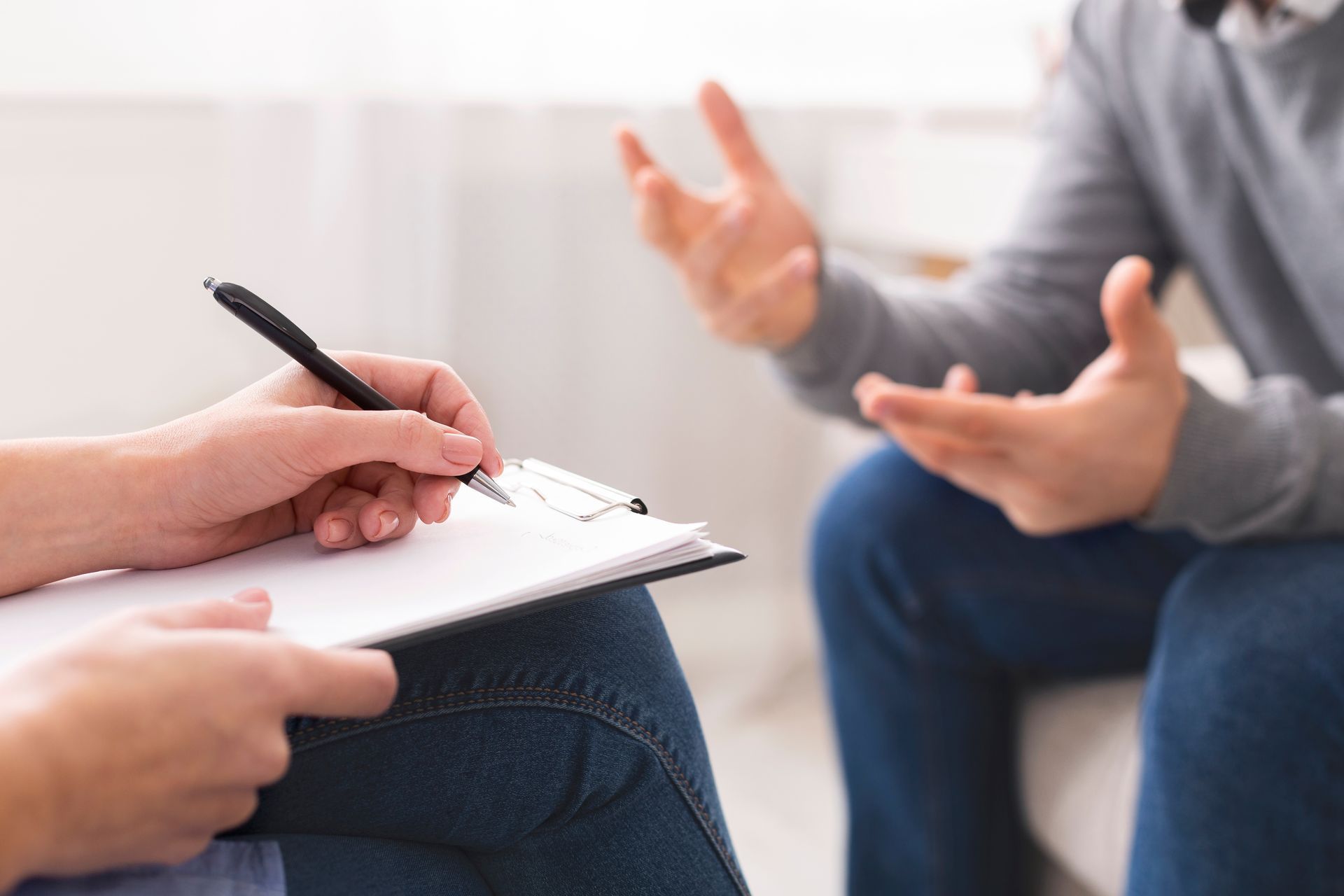 Une femme allongée sur un canapé discute tandis qu'une autre personne est assise, floue en arrière-plan.