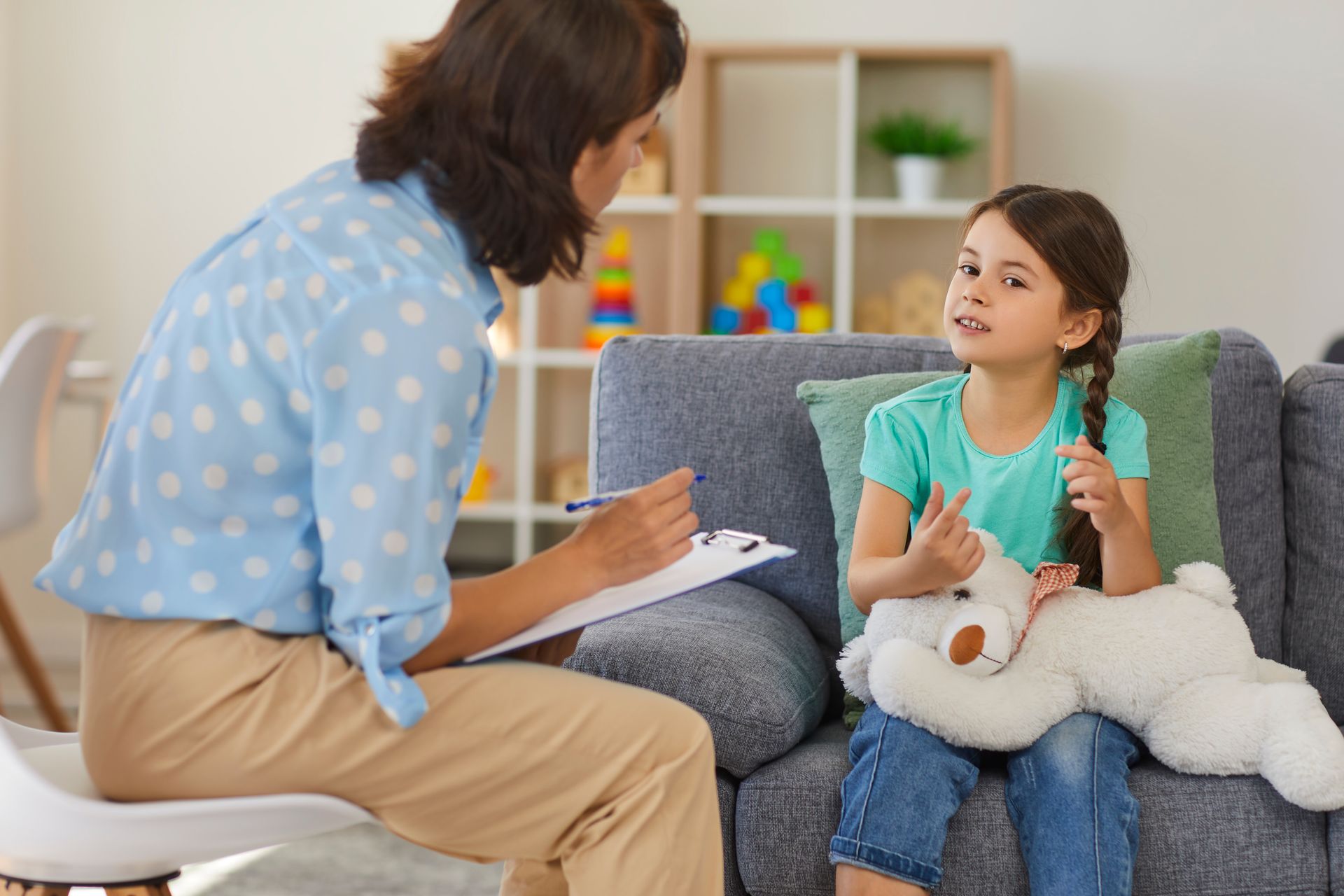 Une femme discute avec une jeune fille sur un canapé tout en prenant des notes dans un salon lumineux.