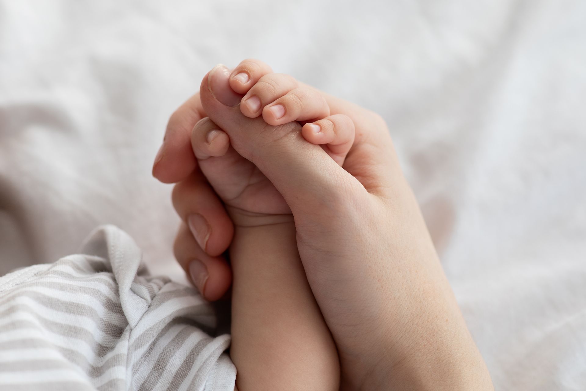 Gros plan une main tenant délicatement la main d'un bébé sur une couverture blanche