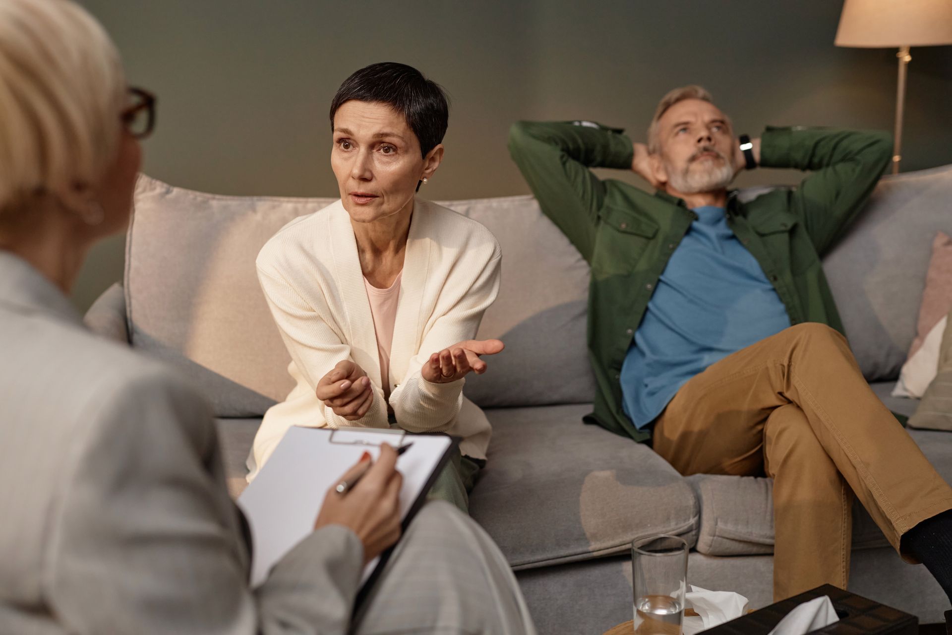Un thérapeute écoute un couple en séance de thérapie sur un divan, une personne parlant tandis que l'autre est adossée.