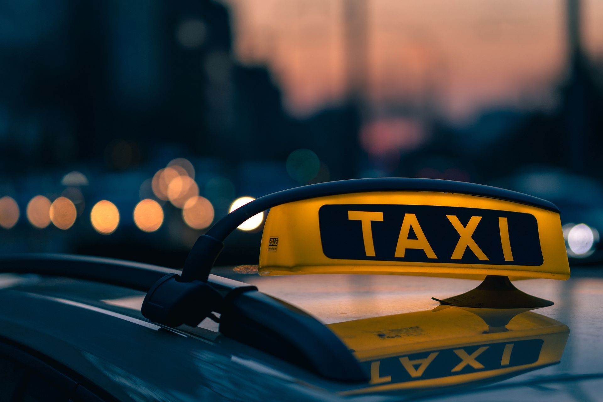 Panneau jaune de taxi sur le toit d'une voiture au crépuscule, avec les lumières floues de la ville en arrière-plan.