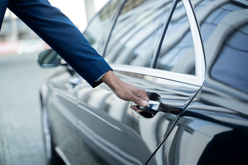 Une personne en veste bleue ouvre la portière argentée d'une voiture par la poignée.