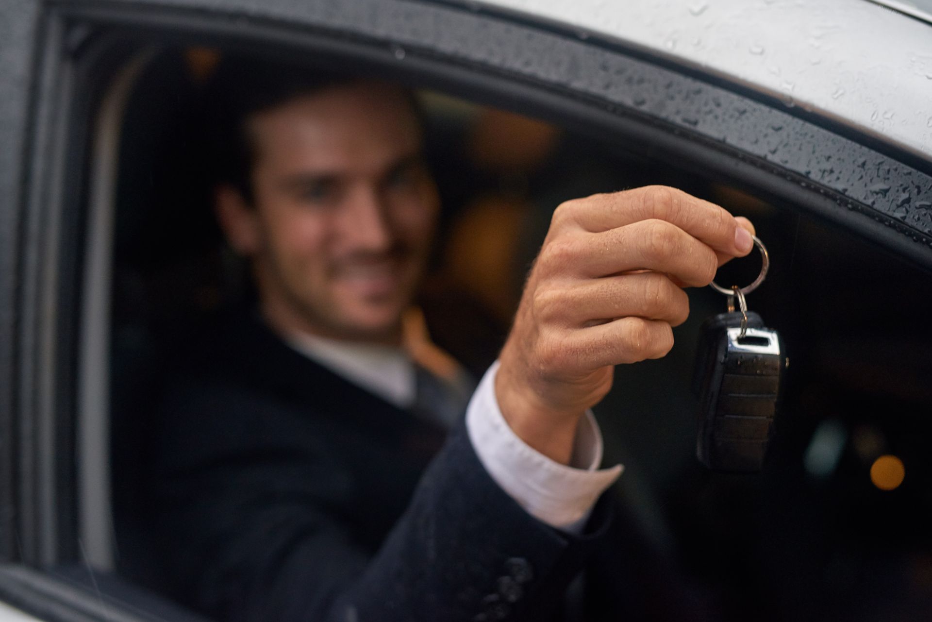 Une personne en costume tient des clés de voiture par la fenêtre.