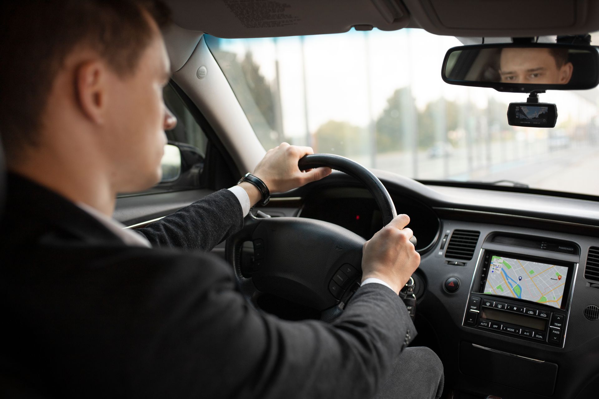 Un conducteur au volant, vu depuis la banquette arrière, avec un écran de navigation GPS visible.