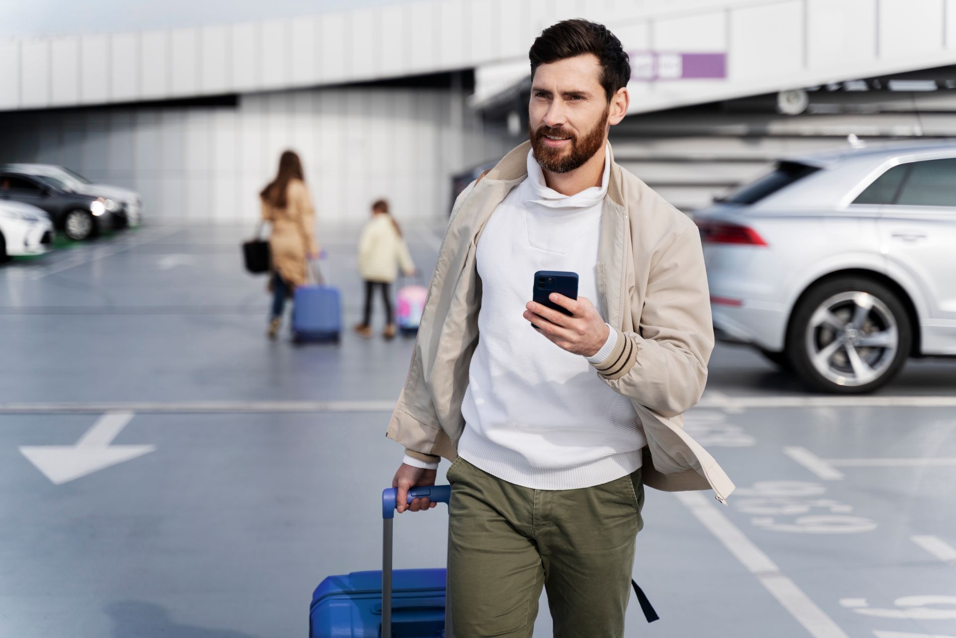 Voyageur avec valise et téléphone dans un parking d'aéroport, voitures et personnes en arrière-plan
