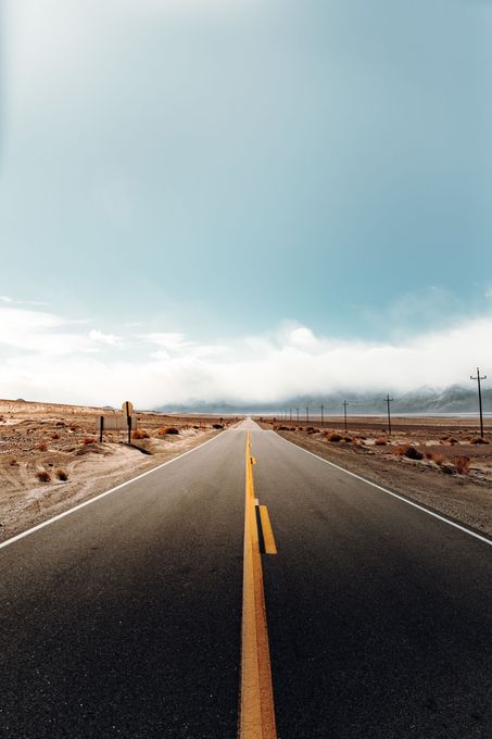Route désertique s'étendant vers l'horizon sous un ciel bleu nuageux