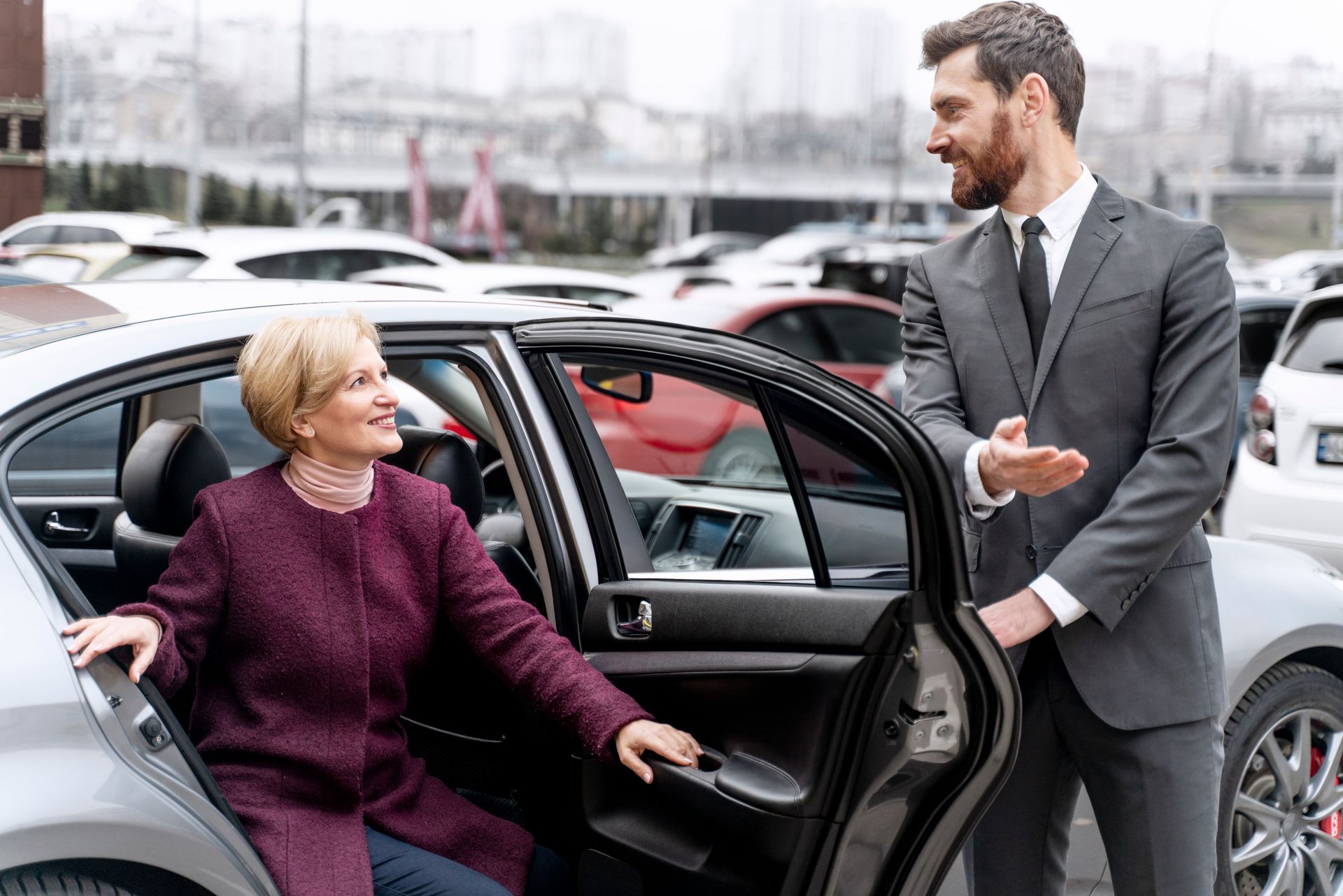 Une femme sort d'une voiture noire tandis qu'un homme en costume lui tient la portière ouverte à l'extérieur.