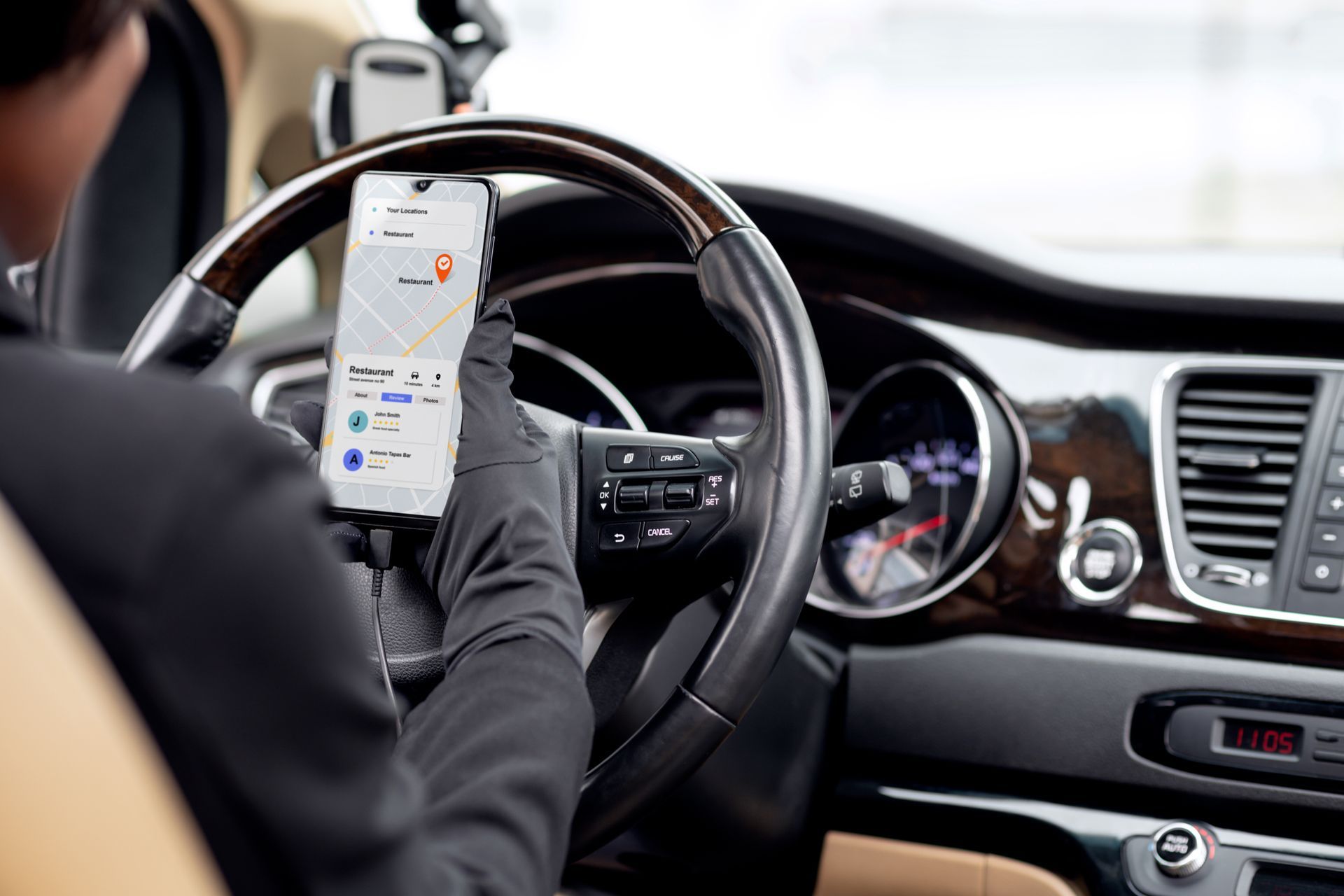 Une personne conduisant en utilisant un smartphone au volant, une main gantée posée sur le volant.