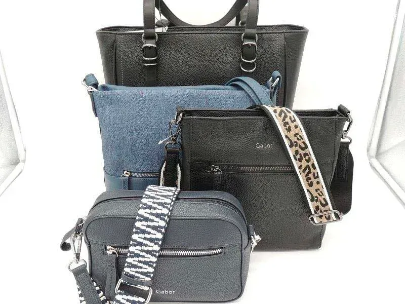 Fünf Handtaschen in Schwarz, Blau und Grau, die in einem Studio-Setting mit gemusterten Riemen übereinander gestapelt sind.