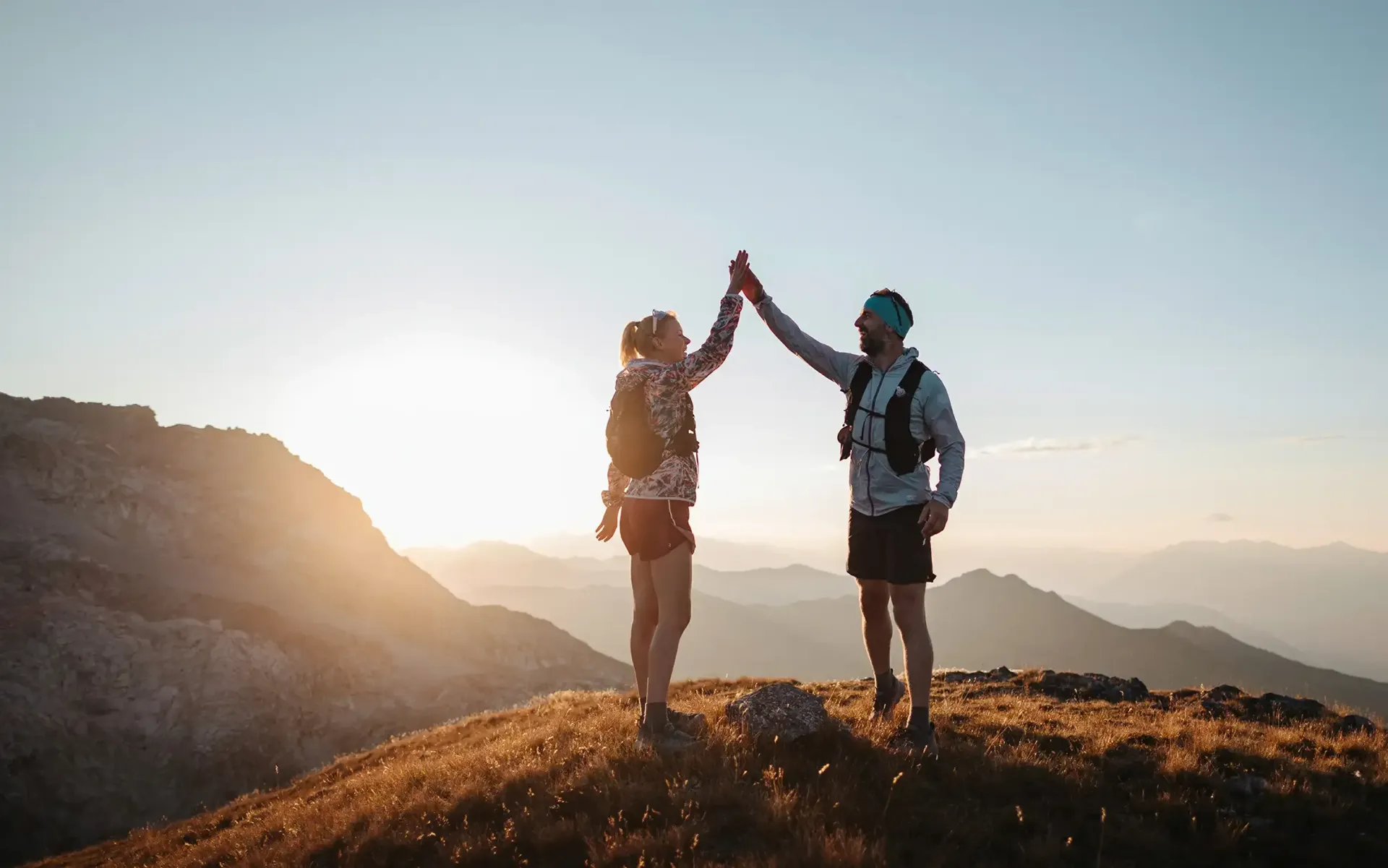 Zwei Wanderer geben sich bei Sonnenaufgang auf einem Bergrücken ein High-Five