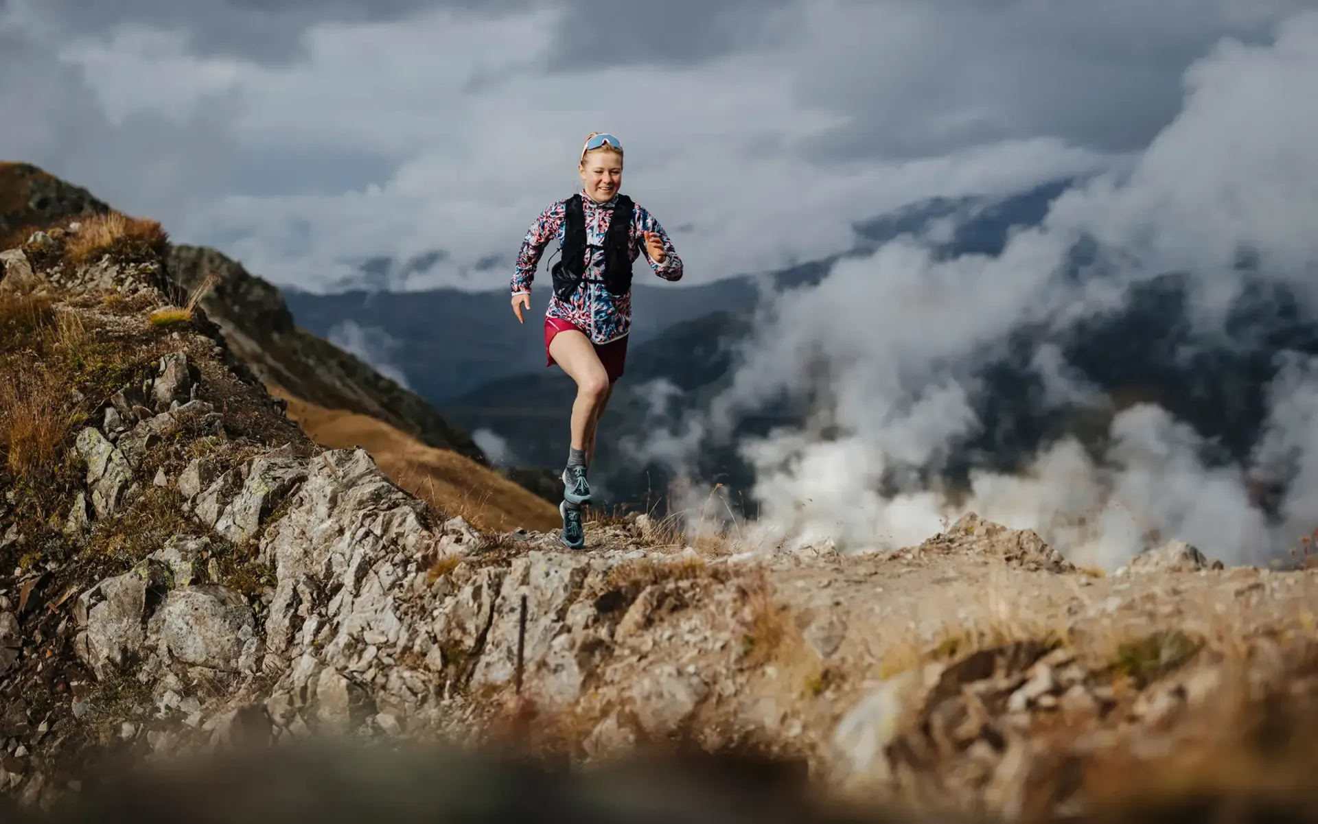 Läufer auf einem felsigen Bergkamm über den Wolken, mit gestreifter Jacke und Rucksack