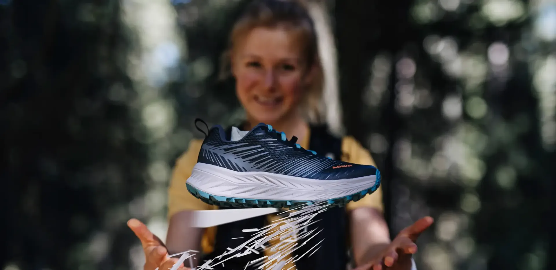 Ein blauer Laufschuh schwebt über gewölbten Händen; im Hintergrund sind eine verschwommene Person und Bäume zu sehen.