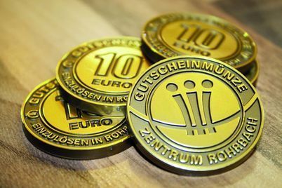 Goldene Euro-Münzen auf einer Holzoberfläche, eine Münze ein markantes „100“ und eine andere das Design „Münzen“ zeigt.