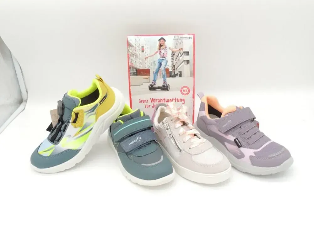Vier Kindersneaker in Blau, Grün, Weiß und Lavendel, arrangiert neben einem Schuhkarton auf weißem Hintergrund